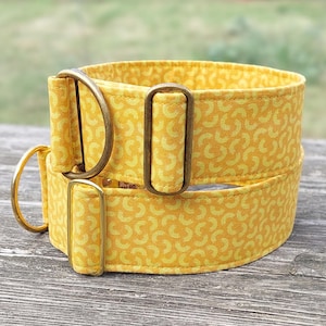 Peut inclure: Un collier jaune pour chien avec un motif répété de petites formes courbes jaune clair. Le collier est doté d'une boucle et d'anneaux en métal de couleur laiton. Le collier est en tissu et semble neuf.