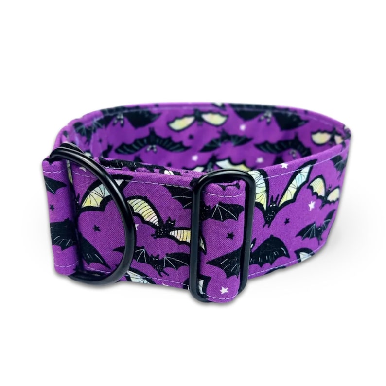 May include: A purple fabric collar featuring a repeating pattern of black bats with yellow and white wing accents and small white stars. The collar includes a black metal D-ring and a black metal rectangular slide adjuster for size adjustment.