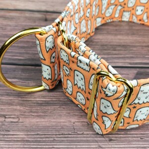 May include: A bright orange dog collar with a white ghost pattern and gold metal hardware. The collar is made of fabric and has a buckle closure.