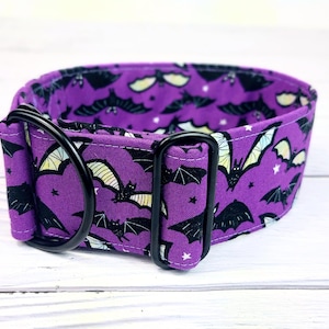May include: A purple pet collar featuring a repeating pattern of black bats with yellow and white wing accents and small white stars. The collar includes a black metal D-ring and a black metal adjustable slider for securing the fit around the neck.