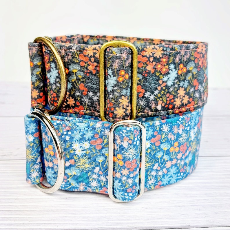 May include: Two dog collars with floral patterns. The top collar is black with orange and pink flowers. The bottom collar is blue with white and orange flowers. Both collars have brass and silver hardware.
