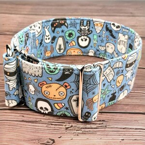 May include: A blue dog collar with a Halloween-themed print featuring ghosts, skeletons, mummies, and other spooky characters. The collar has a silver buckle.