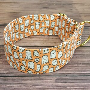 May include: Orange and white dog collar with a pattern of cute ghosts. The collar has a gold metal D-ring.