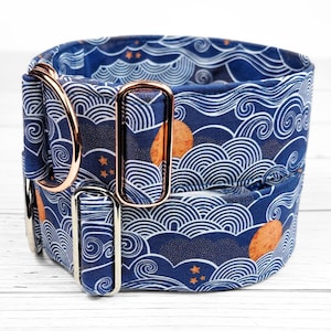 May include: A blue and white dog collar with a wave pattern and gold accents. The collar has two metal D-rings and a buckle.