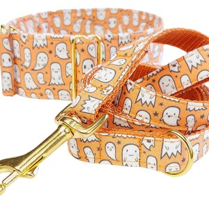 May include: Orange and white dog collar and leash set with a ghost pattern. The collar and leash are made of fabric and have gold metal hardware.