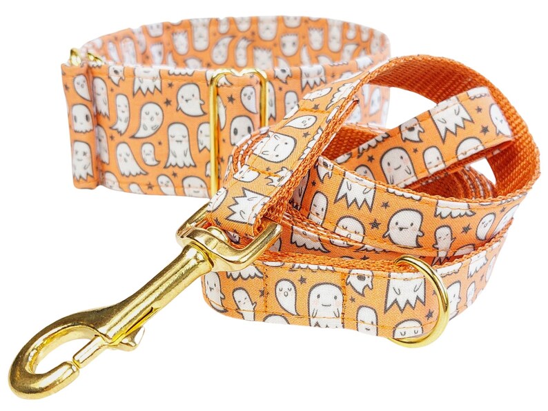 May include: Orange and white dog collar and leash set with a ghost pattern. The collar and leash are made of fabric and have gold metal hardware.