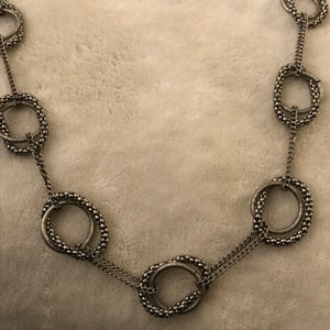 May include: A silver necklace with multiple linked circles, each circle is made of small beads.