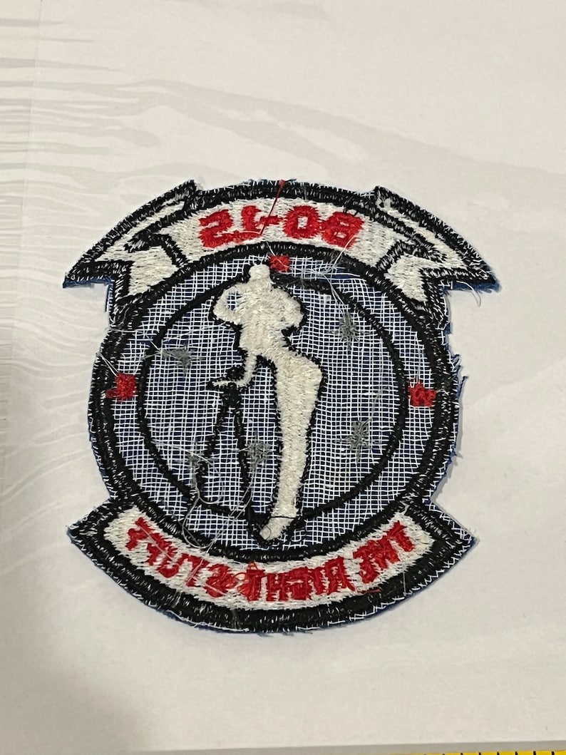 Pu&ograve; includere: Una toppa ricamata blu e bianca con una silhouette bianca di una donna che tiene un fucile. La toppa ha un bordo nero e il testo "808th" e "AIRBORNE" in rosso.