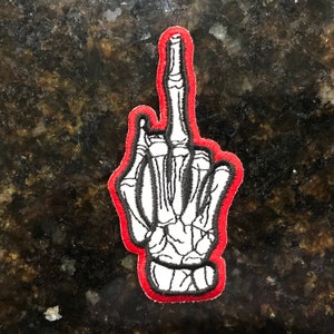 May include: A white skeleton hand giving the middle finger, outlined in red. The hand is embroidered on a patch.