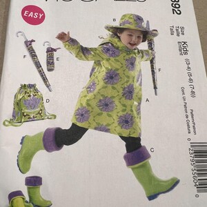 May include: McCall's M6392 sewing pattern for kids' rainwear. The pattern includes a raincoat, hat, boots, umbrella, and drawstring bag. The rainwear features a green floral design with purple accents. Sizes (3-4) (5-6) (7-8).