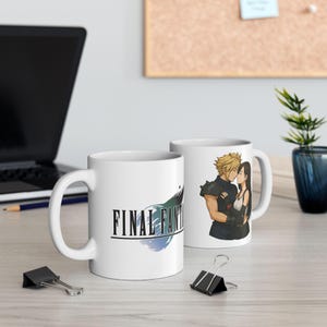 Pode incluir: Duas canecas de cerâmica brancas. Uma caneca apresenta o logotipo "Final Fantasy" em preto e verde-azulado. A outra caneca mostra um casal se beijando. Um laptop, clipes e uma planta estão no fundo.