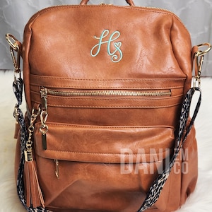 May include: A brown faux leather backpack with a gold zipper and a leopard print strap. The backpack has a monogram of "HS" in light blue thread on the front.