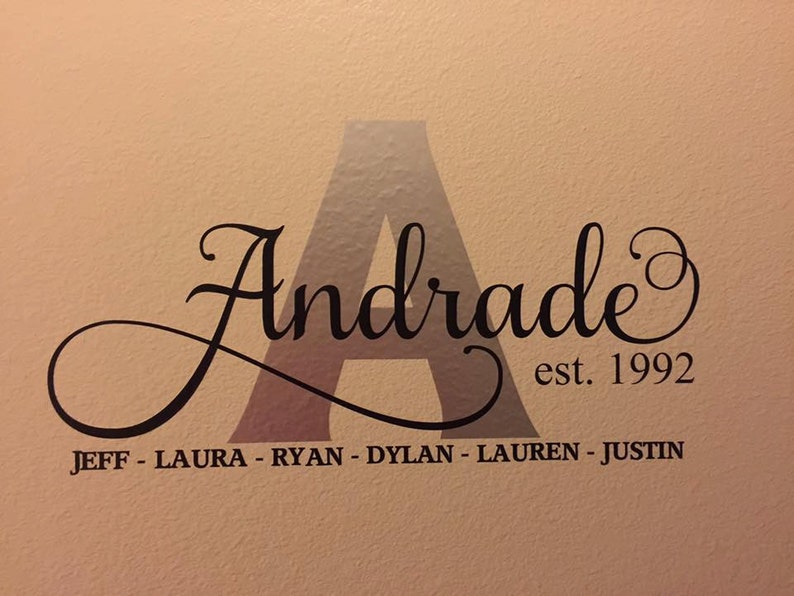 May include: A black and white wall decal with the word "Andrade" in a cursive font, with a large letter "A" in the center. The text "est. 1992" is below the word "Andrade". Below that, the names "JEFF - LAURA - RYAN - DYLAN - LAUREN - JUSTIN" are listed.