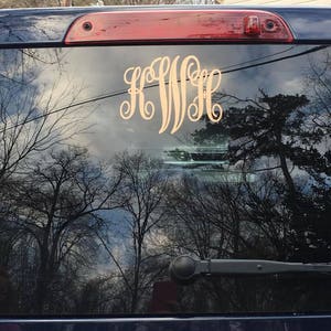 May include: A black car with a gold monogram sticker on the rear window. The monogram is "KWH".
