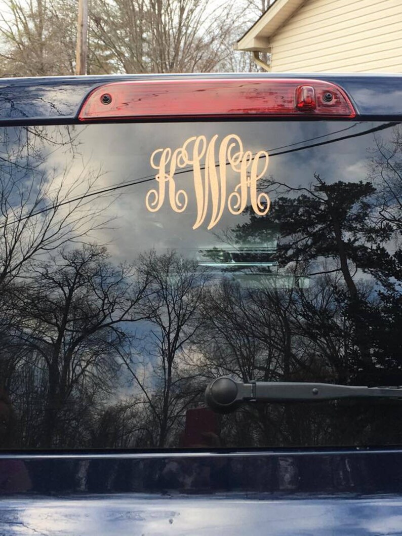 May include: A black car with a gold monogram sticker on the rear window. The monogram is "KWH".