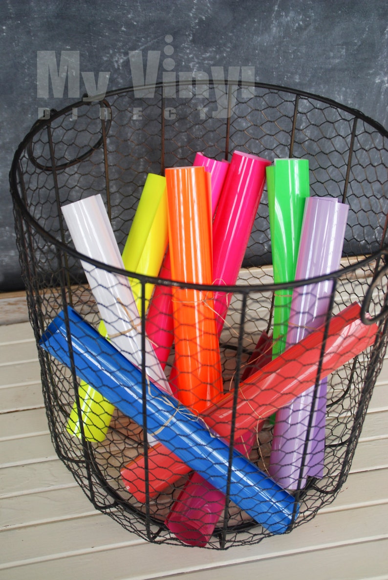 K&ouml;nnte beinhalten: Ein Drahtkorb gef&uuml;llt mit Rollen von farbigem Vinyl in verschiedenen Blaut&ouml;nen, Rot, Rosa, Orange, Gelb, Gr&uuml;n und Lila. Der Korb steht auf einer wei&szlig;en Holzoberfl&auml;che.