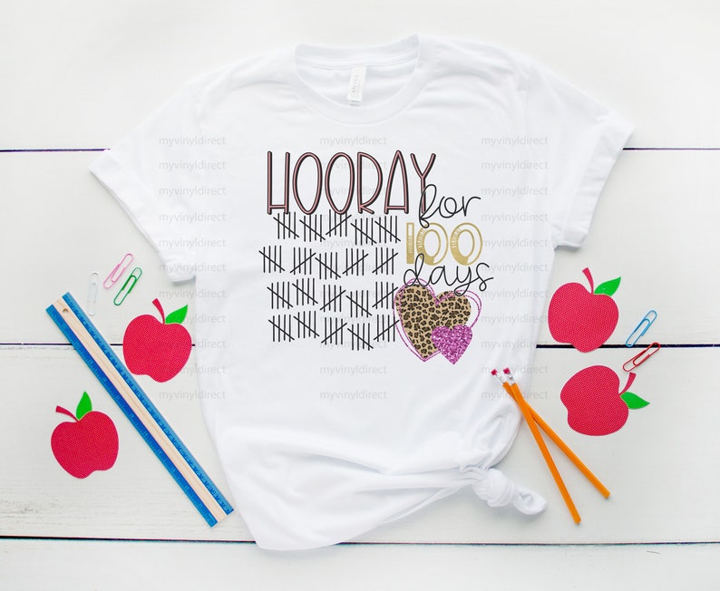 May include: White t-shirt with the text "HOORAY for 100 days" in pink and gold lettering. The text is surrounded by a grid of black lines and two pink and gold hearts. One heart has a leopard print pattern.