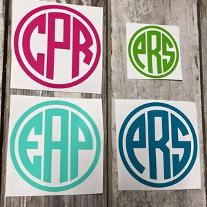 May include: Four round stickers with white backgrounds and black outlines. Each sticker features a different set of three letters in a circle. The letters are in a bold, sans-serif font. The stickers are in the colours pink, green, turquoise, and blue.