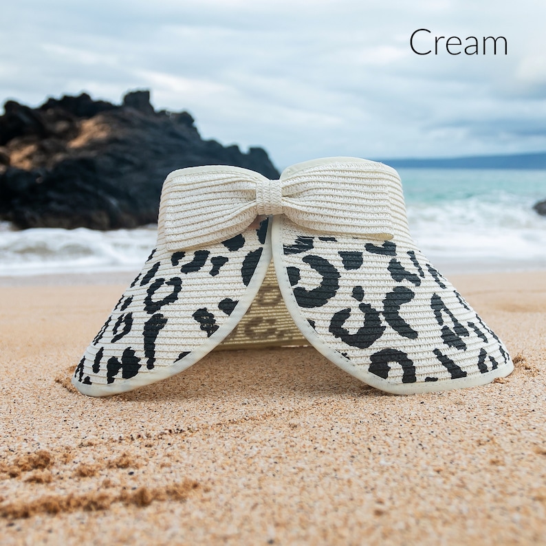 Puede incluir: Sombrero de sol de color crema con un dise&ntilde;o de estampado de leopardo en blanco y negro. El sombrero tiene un gran lazo en la parte superior y est&aacute; hecho de paja.