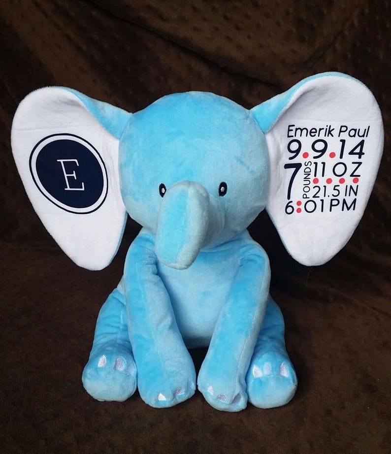 K&ouml;nnte beinhalten: Ein blauer Pl&uuml;sch-Elefant mit wei&szlig;en Ohren und einem wei&szlig;en Fleck auf seinem rechten Ohr. Der Fleck hat den Buchstaben "E" in einem dunkelblauen Kreis und den Text "Emerik Paul 9.9.14 7 Pfund 11 oz 21.5 in 6:01 PM".
