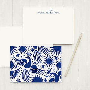 May include: A set of two white note cards with blue floral designs. The top card has the name "anna catherine" printed in blue ink. The bottom card has a blue floral design with peacocks.