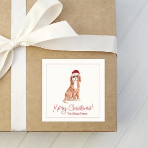 May include: A wrapped gift box with a white ribbon and a square sticker. The sticker features a watercolor illustration of a dog wearing a Santa hat, with the text "Merry Christmas!" and a family name.