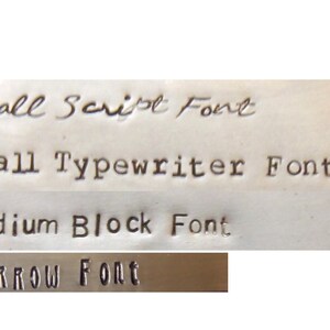 May include: A metal surface displaying four distinct stamped font styles. The text reads Small Script Font, Small Typewriter Font, Medium Block Font, and Narrow Font. Each line demonstrates a different typeface style impressed into the metallic material.
