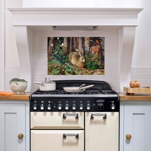 Könnte beinhalten: Eine Küche mit einem schwarz-cremefarbenen Herd und einem Gemälde eines Hasen in einer Waldszene darüber. Ein Sieb mit Brokkoli und eine Karotte stehen auf der Arbeitsplatte. Ein weißer Topf und eine Pfanne stehen auf dem Herd.