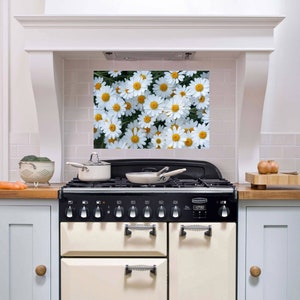 May include: A white kitchen with a white range and a backsplash featuring a daisy pattern. The range has a black top and black knobs. There are two pots on the stovetop.