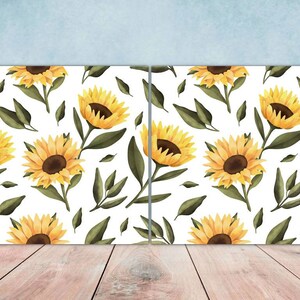 Può includere: Due tele con sfondo bianco e un motivo ripetuto di girasoli gialli con foglie verdi.