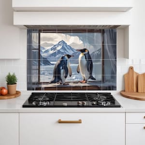 Puede incluir: Un protector contra salpicaduras de cocina con una pintura de dos pingüinos de pie en un alféizar, con vistas a un paisaje montañoso nevado. Los pingüinos son negros, blancos y amarillos. El fondo muestra una cordillera nevada y un mar helado.