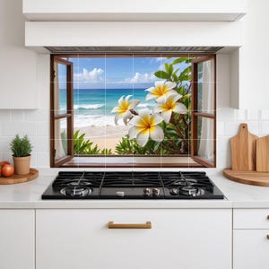Puede incluir: Un protector contra salpicaduras de cocina con una vista de ventana de una escena de playa tropical. La ventana abierta revela un océano azul, arena blanca y flores blancas y amarillas. La cocina tiene una encimera negra y gabinetes blancos.