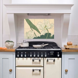 Może przedstawiać: Kuchnia z czarną i kremową kuchenką oraz białym okapem. Nad kuchenką mural z płytek przedstawia białe kwiaty lotosu i zielone liście. Na blacie durszlak z brokułami i rondel.
