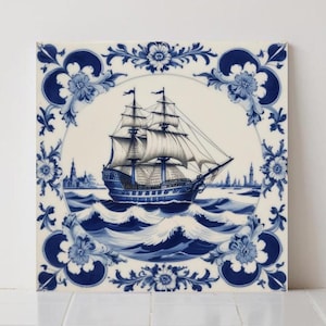 Op de afbeelding: Vierkante keramische tegel met een blauw-witte illustratie van een zeilschip op zee. Het schip is omlijst door een bloemenrand. De tegel meet ongeveer 15 cm vierkant.