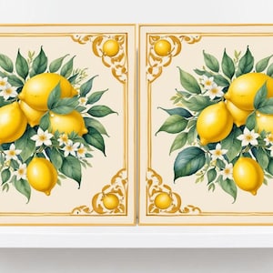 May include: Two framed art prints with watercolour illustrations of lemons, green leaves, and white flowers. The artwork has a cream background with gold decorative borders. The lemons are yellow and the leaves are green.