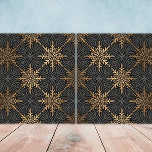 May include: Two black square canvases with a gold intricate pattern. The pattern is a repeating design of stylized flowers.