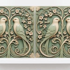 Op de afbeelding: Twee keramische tegels met een reliëfdesign van gestileerde vogels en bloemtakken. De vogels zijn lichtgroen en wit, en de takken zijn groen en crème. De achtergrond is lichtgroen.