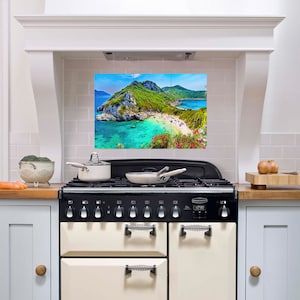 Puede incluir: Una cocina blanca con una cocina de gama negra y crema. El salpicadero está alicatado y presenta una imagen panorámica de una isla tropical con una playa y agua turquesa.