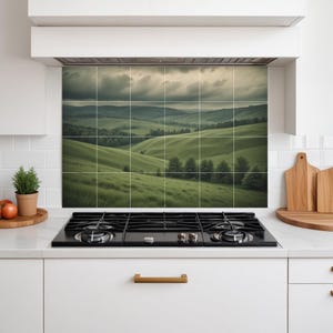 Peut inclure: Un dosseret de cuisine carrelé représentant un paysage de collines verdoyantes sous un ciel nuageux. L'image est divisée en carreaux carrés et est installée au-dessus d'une table de cuisson noire.