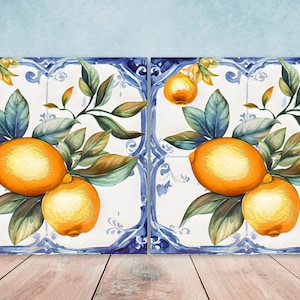Può includere: Due piastrelle quadrate in ceramica con un bordo blu e bianco. Ogni piastrella presenta un dipinto ad acquerello di un ramo di limone con foglie verdi e limoni gialli.