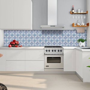 Puede incluir: Una cocina blanca con una estufa de acero inoxidable y un salpicadero de azulejos azul y blanco. Hay un estante de madera con copas de vino y una planta en la encimera.