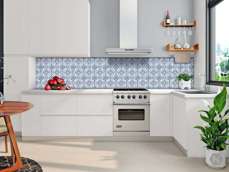 Puede incluir: Una cocina blanca con una estufa de acero inoxidable y un salpicadero de azulejos azul y blanco. Hay un estante de madera con copas de vino y una planta en la encimera.
