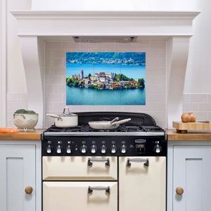 Puede incluir: Una cocina blanca con una cocina de color crema con detalles negros y un salpicadero con una imagen panorámica de una pequeña isla con edificios y árboles en un lago.