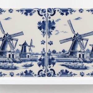 May include: Two blue and white Delft tiles depicting windmills in a Dutch landscape. The tiles are framed with a floral design.