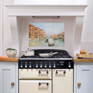 May include: A white kitchen with a black and cream range stove. The backsplash is tiled with a scenic image of a canal in Venice, Italy.