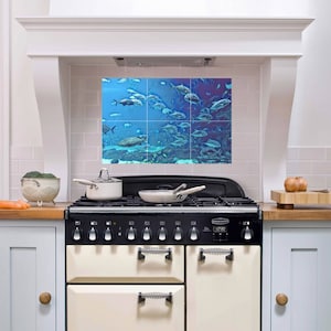 May include: A white kitchen with a black and cream range oven. The backsplash is a tiled mural of a school of fish swimming in blue water.
