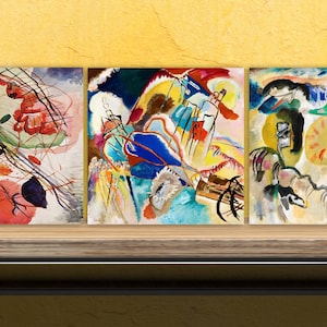 May include: Three abstract paintings in a modern style, with a mix of colours including red, blue, yellow, green, and white. The paintings are displayed on a wooden shelf against a yellow wall.