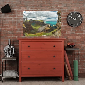May include: A red three-drawer dresser with black knobs against a brick wall background. A framed landscape photograph of a rocky coastline with a blue ocean hangs above the dresser. A black clock with white hands is on the wall to the right of the dresser.