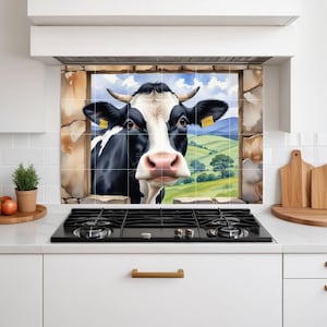 Puede incluir: Un protector contra salpicaduras de cocina con una ilustración caprichosa de una vaca en blanco y negro que mira a través de una ventana de piedra. La cara de la vaca es el punto focal, con un paisaje rural visible en el fondo. El diseño añade un toque de encanto rústico a la cocina.