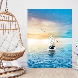 Könnte beinhalten: Leinwanddruck mit einem Segelschiff auf dem Meer unter einem blau-gelben Himmel. Zwei Möwen fliegen über dem Schiff. Der Druck wird in einem Raum mit einem hängenden Korbstuhl ausgestellt.
